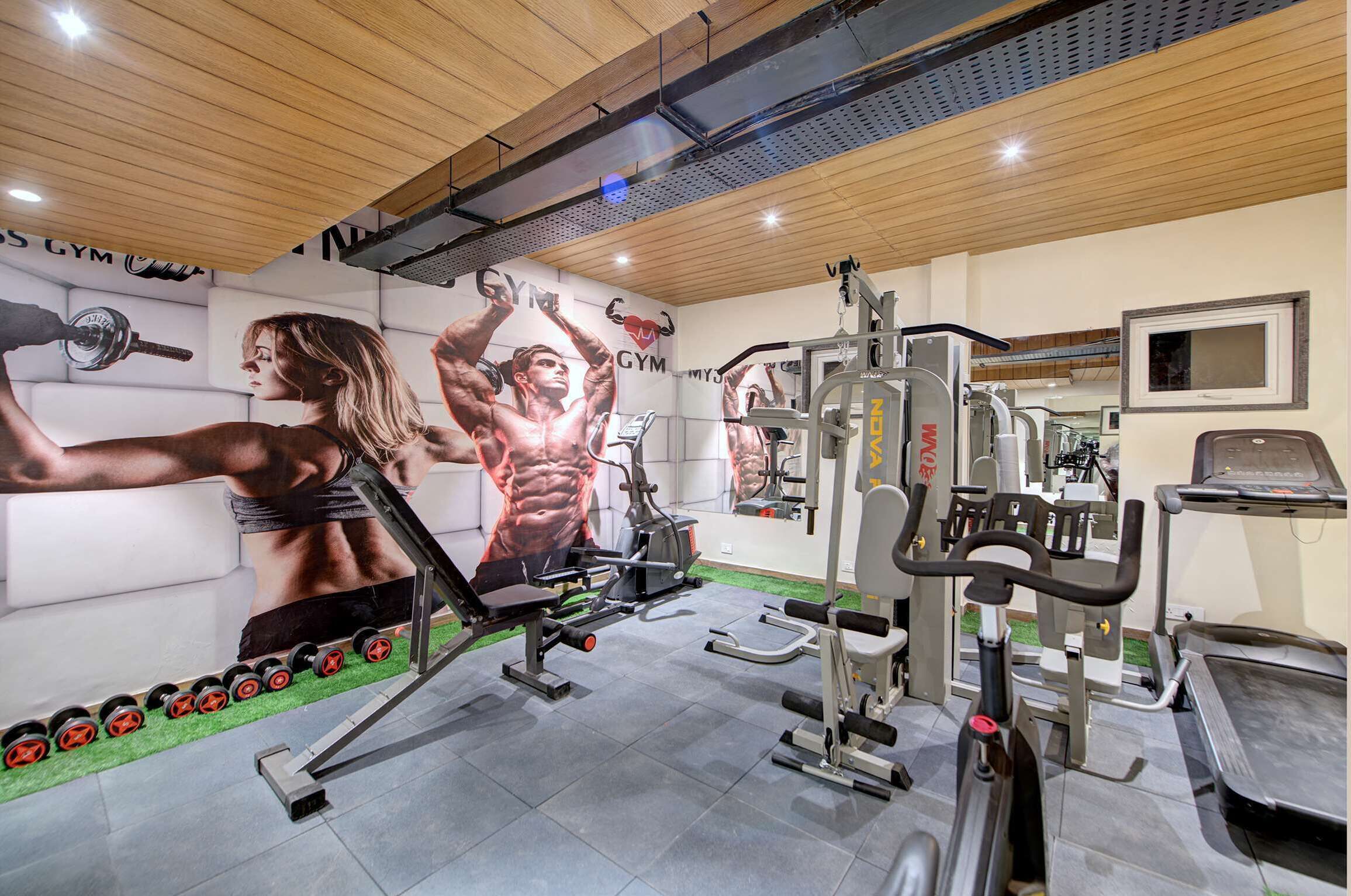 Een sportschool met trainingsapparatuur, een muur met fitnessmuurschilderingen en een houten plafond.