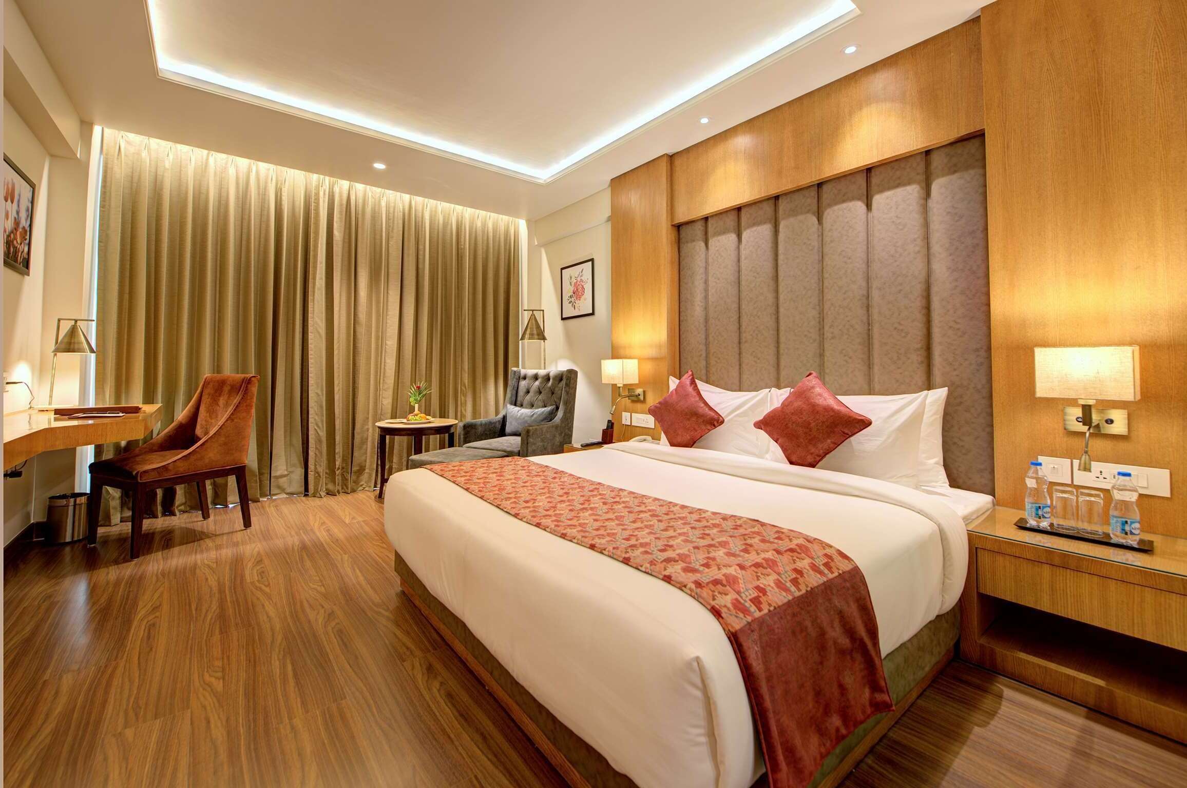Habitación de hotel con una cama grande, un escritorio, una silla y una mesita de noche con lámparas y botellas de agua.