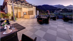 Terraza en la azotea con mesas y sillas, una pérgola y vistas a la montaña.
