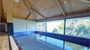 Una amplia piscina interior con techo de madera y vistas a árboles al exterior.
