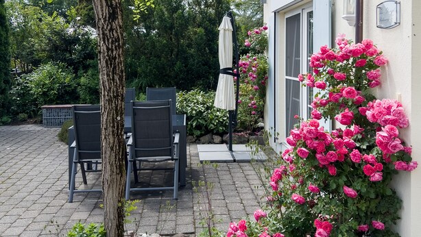 Eine Terrasse mit Gartenmöbeln, einem Baum und blühenden Blumen.