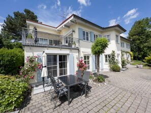 A two-story house with a balcony, a patio with a table and chairs, and a garden with flowers. - Gediegene Eleganz und fantastischer Bergblick in absoluter Ruhe! (Scheidegg)