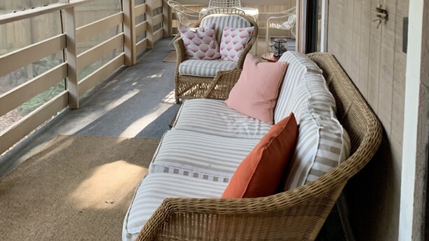 A covered porch with wicker furniture, a cushioned bench, and a wall-mounted clock. - 2+2 Beach Condo (Fernandina Beach)