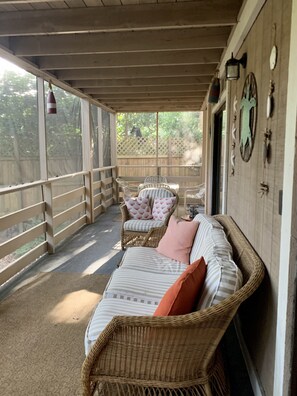 A covered porch with wicker furniture, a cushioned bench, and a wall-mounted clock. - 2+2 Beach Condo (Fernandina Beach)