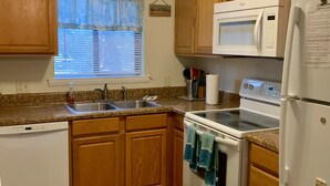 A compact kitchen with wooden cabinets, a built-in microwave, a stove, and a refrigerator. - 2+2 Beach Condo (Fernandina Beach)