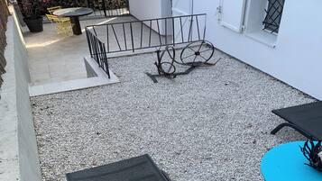 Zona de pati amb taula i cadires, una taula blava i un sòl de grava.