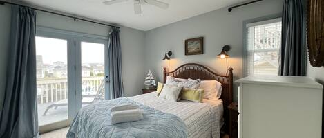 Ein Schlafzimmer mit Bett, Deckenventilator, Nachttisch, Lampe und Blick ins Freie.