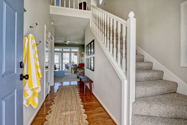 A hallway with a wooden floor, a rug, a staircase with white balusters, and a door with yellow and white striped towels hanging on it.