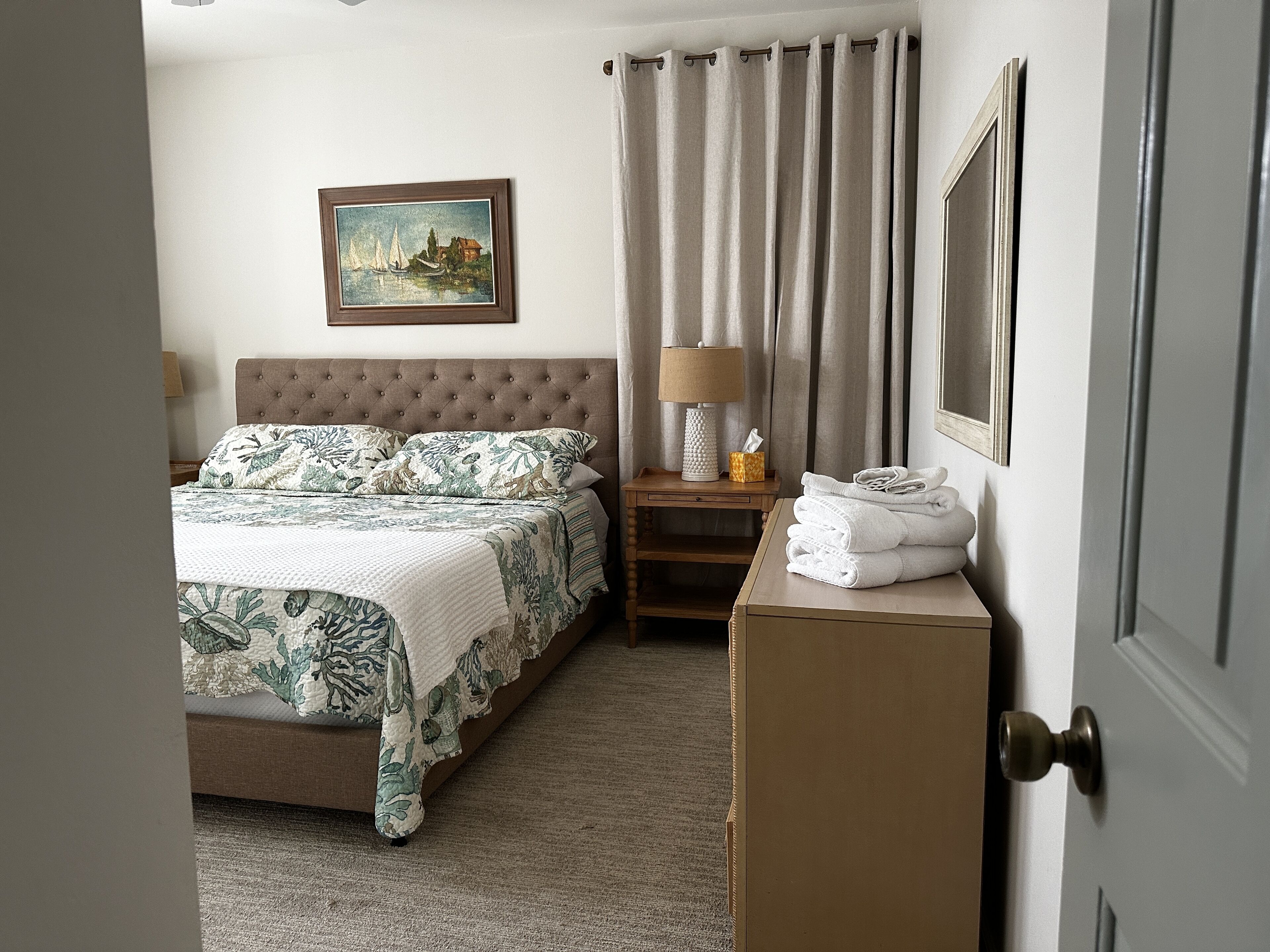 Een keurig opgemaakt hotelkamer met een bed, een nachtkastje met een lamp, een lijst met een foto aan de muur en een deur.