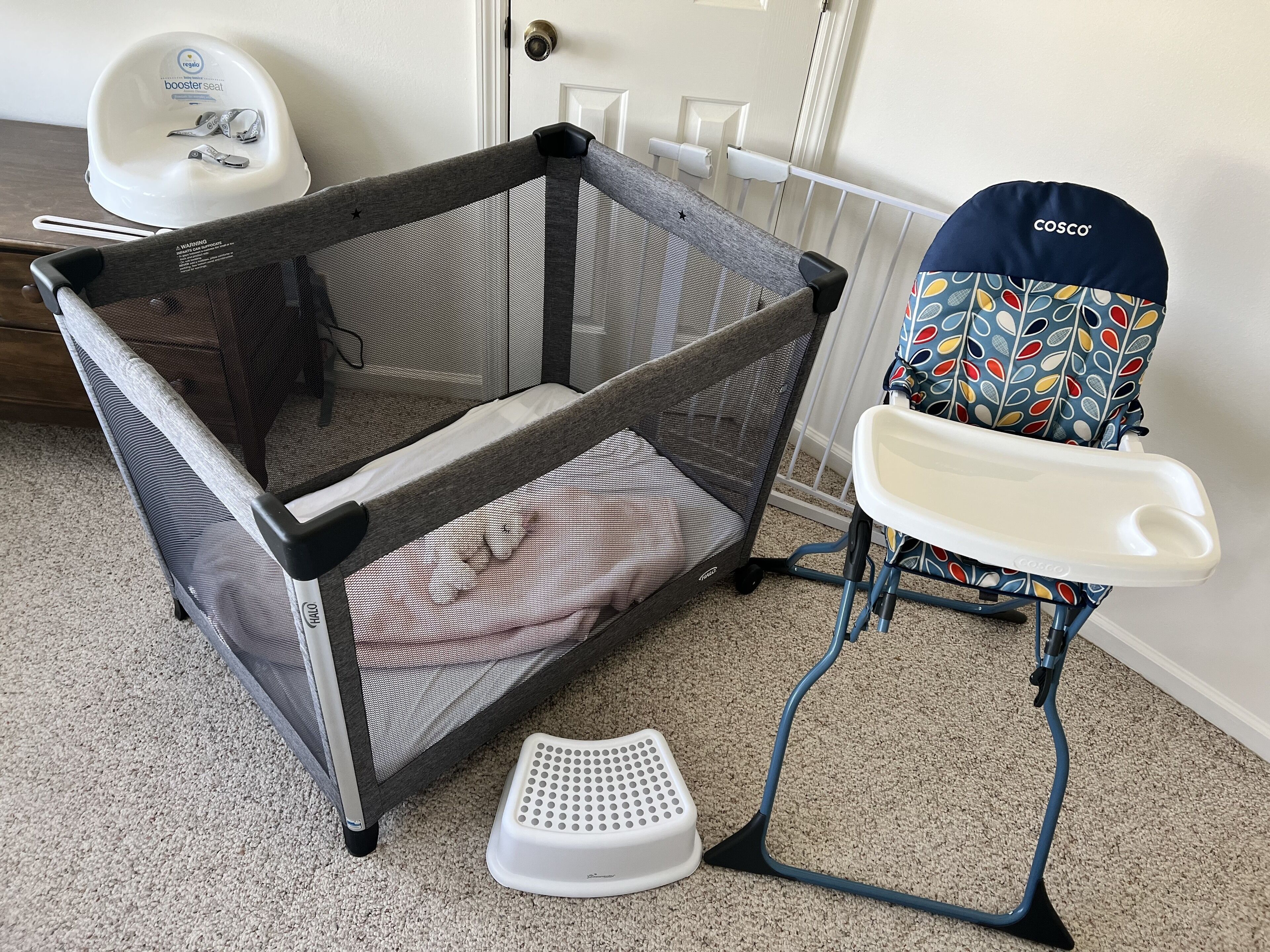 A baby playpen with a mesh top, a baby seat, and a white booster seat.