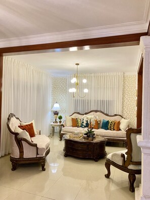 A spacious living room with a sofa, two armchairs, a coffee table, and a chandelier.