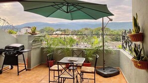 Un balcón con mesa, sillas, una parrilla y plantas en macetas.