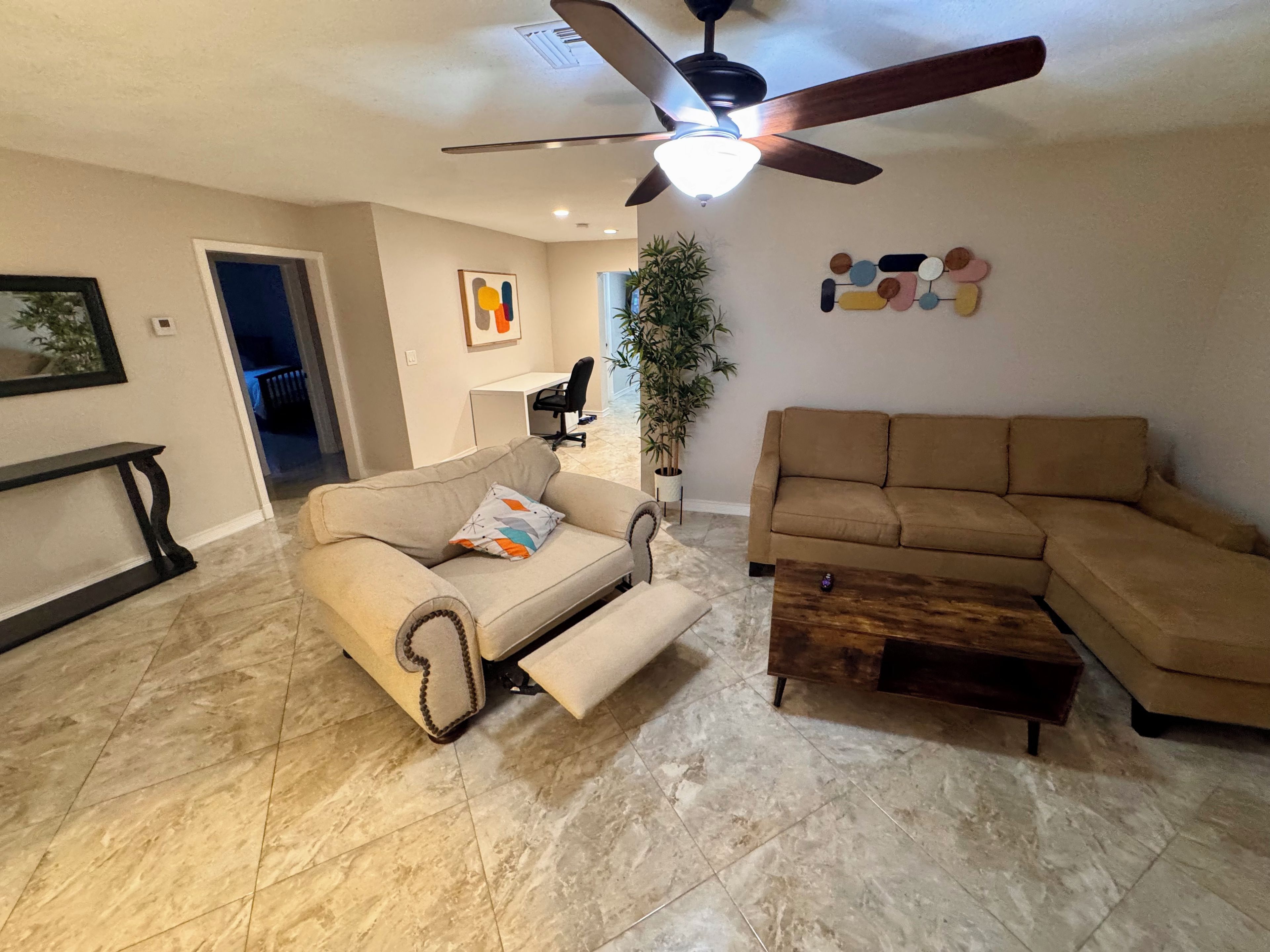 A living room with a sofa, a coffee table, a ceiling fan, and a wall-mounted artwork.