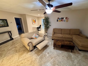 A living room with a sofa, a coffee table, a ceiling fan, and a wall-mounted artwork.