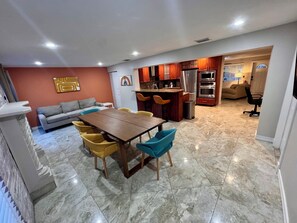 A spacious living area with a dining table and chairs, a sofa, and a kitchen with modern appliances.