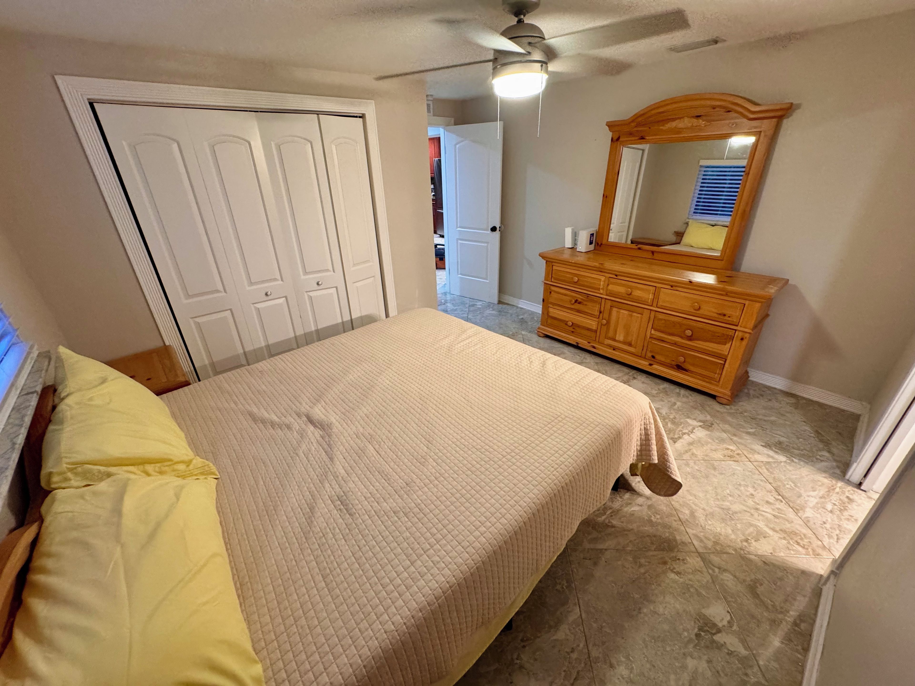 A bedroom with a bed, a dresser, a mirror, and a ceiling fan.