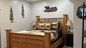 A bedroom with a wooden bed, a ceiling fan, a nightstand, and wall decorations including tree and bear silhouettes.
