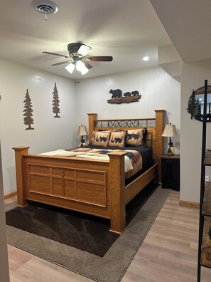 A bedroom with a wooden bed, a ceiling fan, a nightstand, and wall decorations including tree and bear silhouettes.