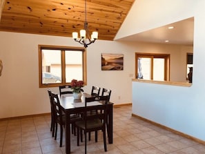 Uma sala de jantar com teto de madeira, um candelabro, uma mesa com cadeiras e uma janela com vista para um carro lá fora.