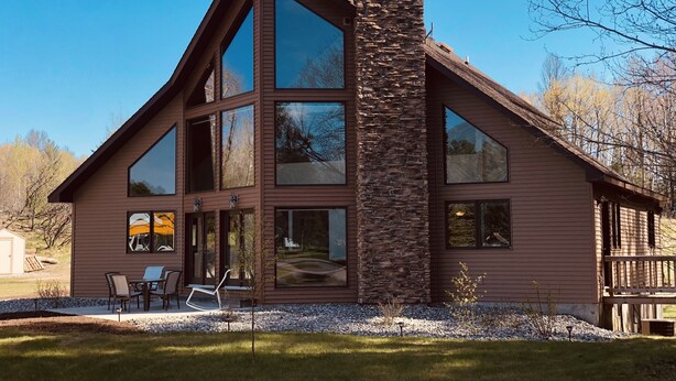 A modern two-story house with large windows, a stone chimney, and a deck.