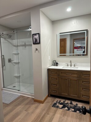 A modern bathroom with a glass shower enclosure, a wooden vanity with a mirror, and a bear-themed rug.
