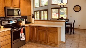 A kitchen with wooden cabinets, a stainless steel stove, a microwave, and a large window overlooking a yard.