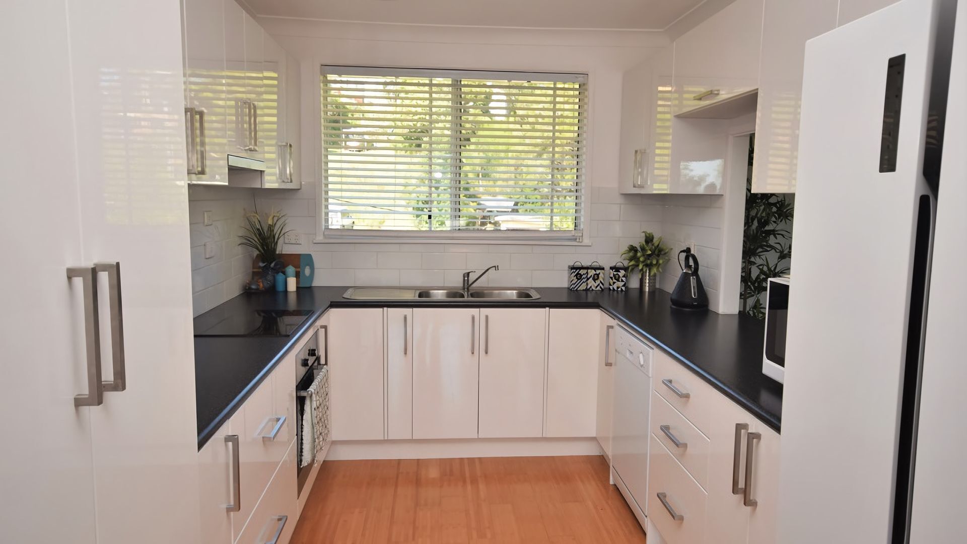A modern kitchen with white cabinetry, a black countertop, and a window with blinds.