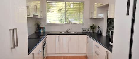 A modern kitchen with white cabinetry, a black countertop, and a window with blinds.