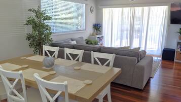 A dining area with a wooden table and white chairs, a grey sofa, and a potted plant.