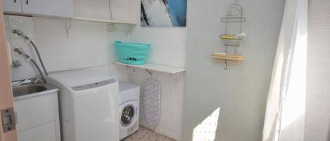 Een kleine wasruimte met een wasmachine, een droger, een wasbak en een wandplank met een mand.