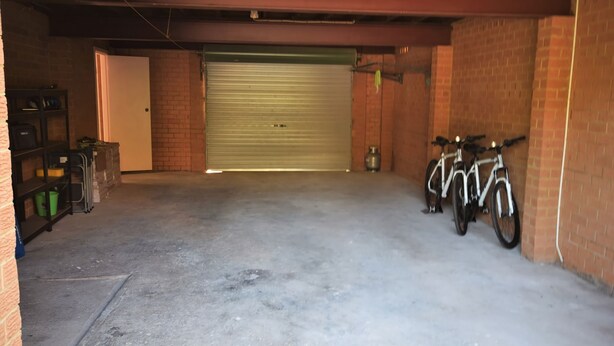A garage with a closed garage door, two bicycles parked against the wall, and a shelving unit with various items.