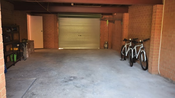A garage with a closed garage door, two bicycles parked against the wall, and a shelving unit with various items.