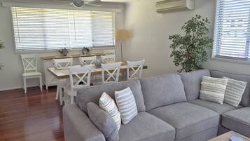 A living room with a grey sofa, white chairs, a dining table, and a potted plant.