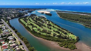 An aerial view of a coastal area with a golf course, a river, and a residential area.