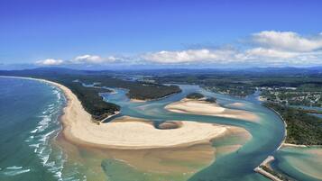 An aerial view of a coastal area with a beach, water channels, and surrounding greenery.