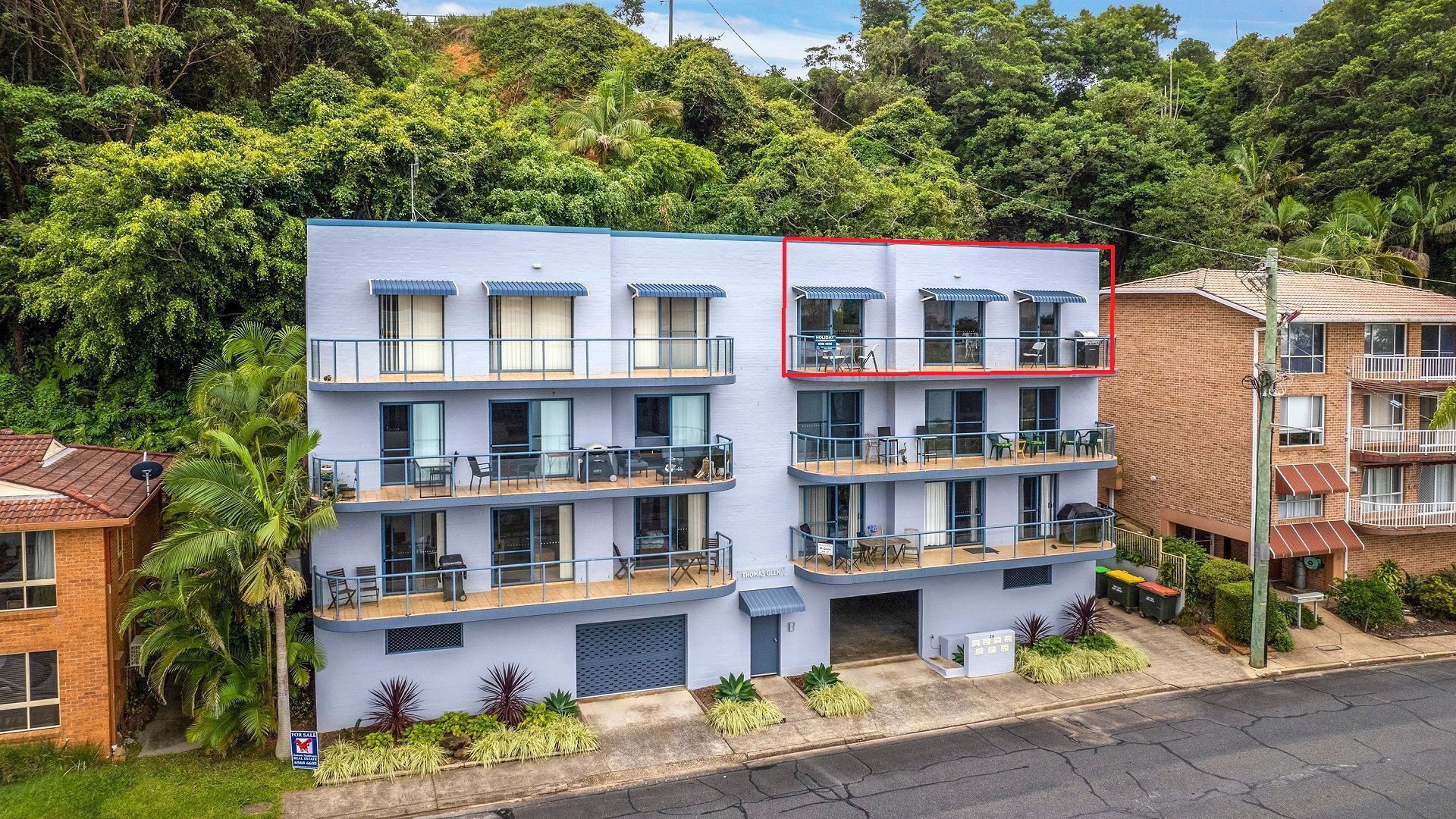 A multi-story building with balconies, a flat roof, and a sign indicating a for sale property.