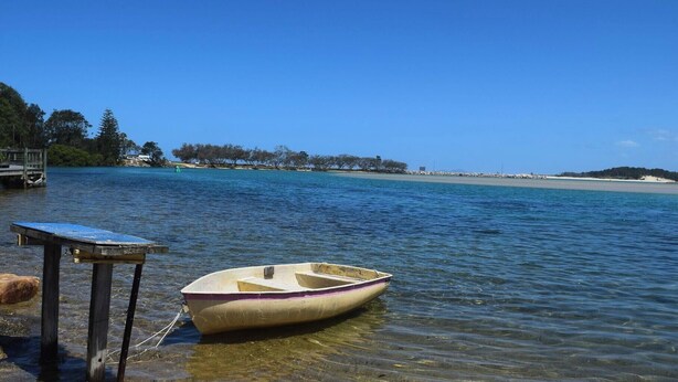 A small boat tied to a dock with clear water and a distant shoreline.