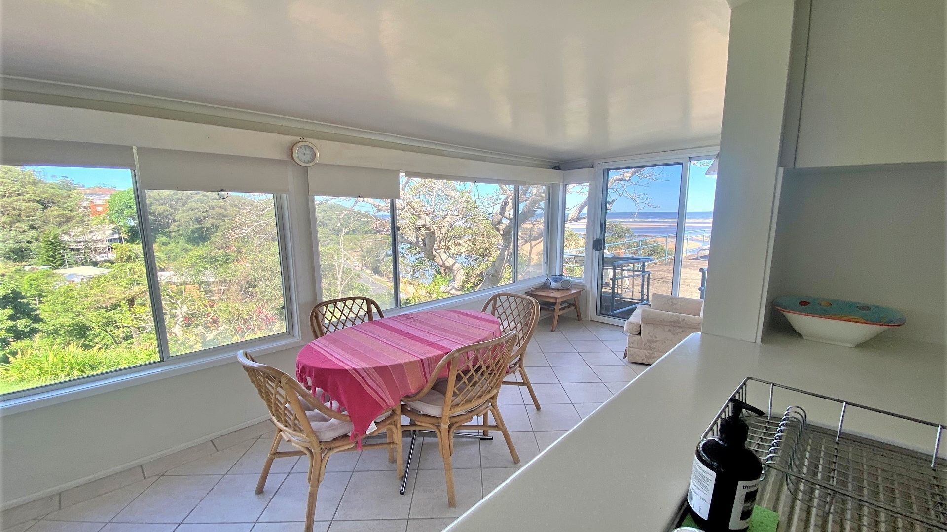 A dining area with a table and chairs, a view of greenery and buildings, and a balcony with a railing.