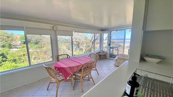 A dining area with a table and chairs, a view of greenery and buildings, and a balcony with a railing.