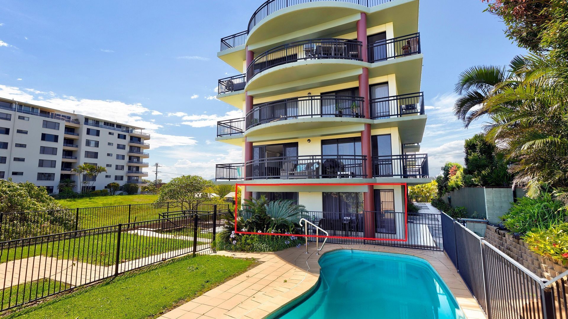 A multi-story hotel with a swimming pool, outdoor seating, and a fenced garden area.