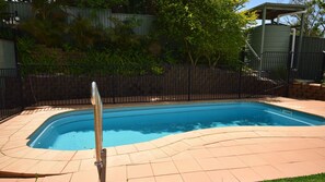 A rectangular swimming pool with a tiled deck, surrounded by a black metal fence, and a stone wall in the background.