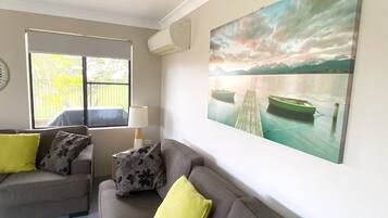 A living room with a grey sofa, two yellow cushions, a lamp, and a large landscape painting of a lake and mountains.