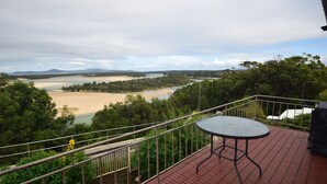 Un balcon avec une table et une balustrade donnant sur une rivière et un paysage boisé.
