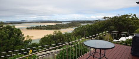 A balcony with a table and railing overlooking a river and forested landscape.