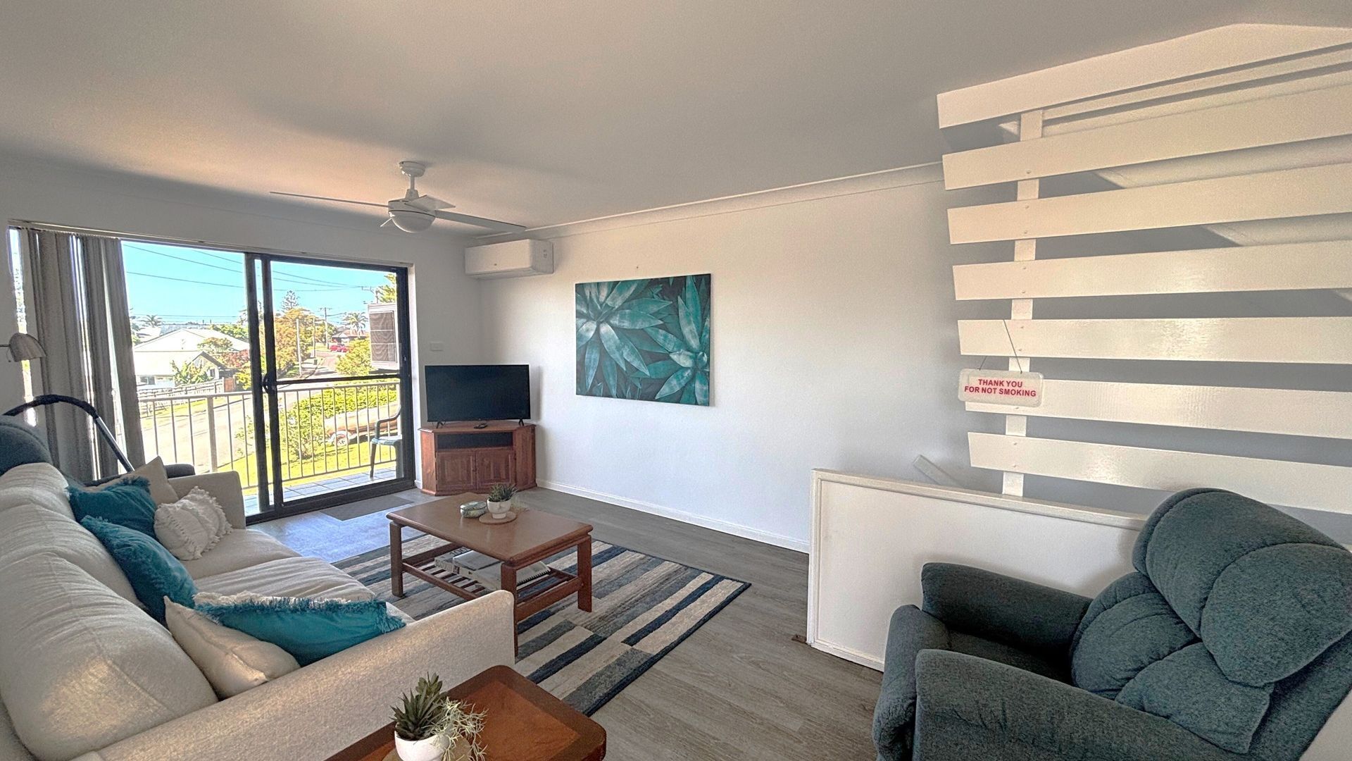 A living room with a sofa, armchair, coffee table, and a flat-screen TV on a stand.