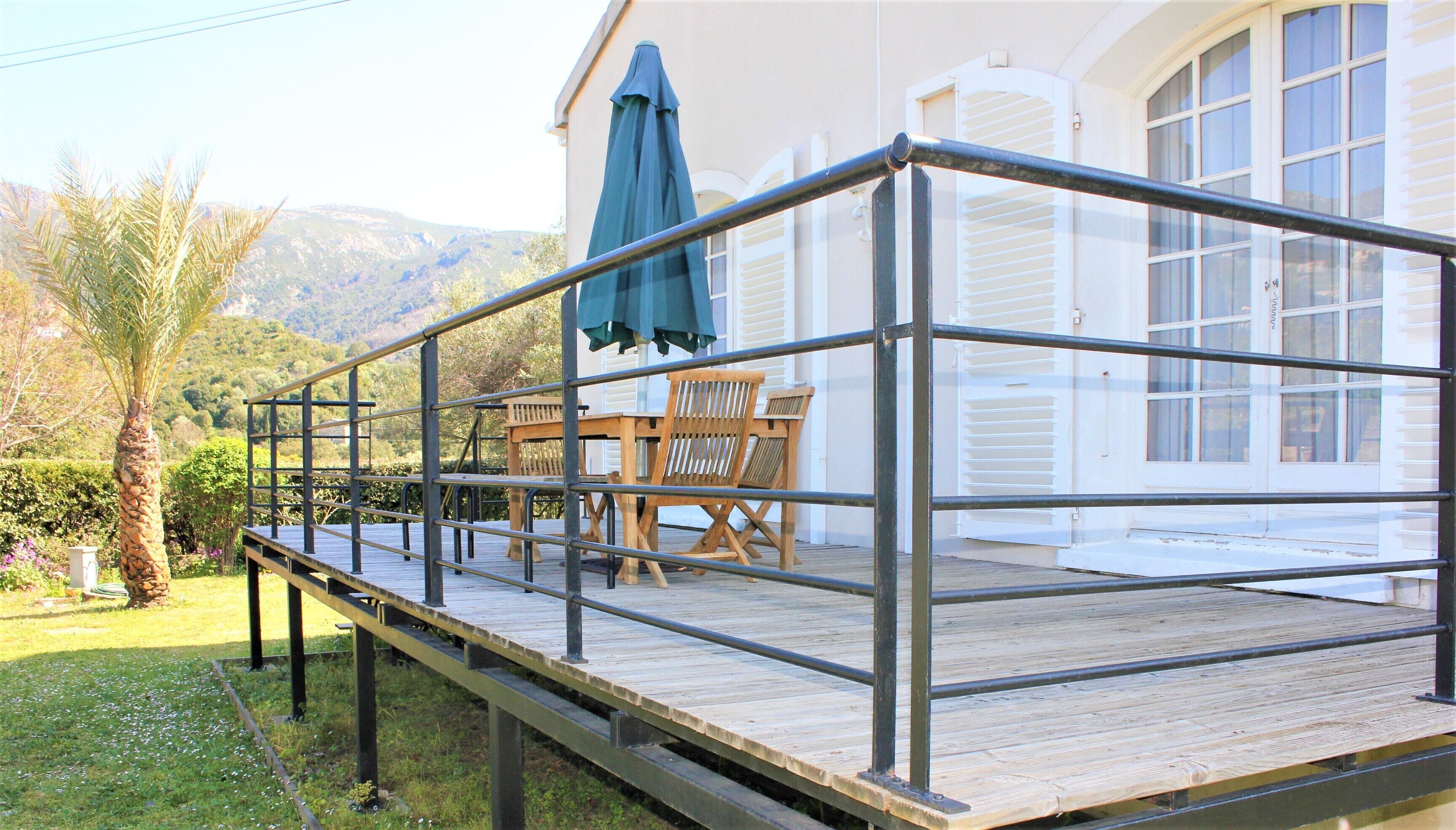 A wooden deck with metal railings, a table with chairs, and a green umbrella.