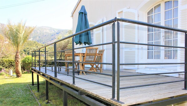 A wooden deck with metal railings, a table with chairs, and a green umbrella.
