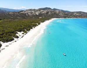 Eine Küstenlandschaft mit einem Sandstrand, klarem türkisblauem Wasser und einem gebirgigen Hintergrund.