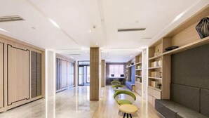 A modern interior with a long hallway, green chairs, a sofa, and built-in shelving.