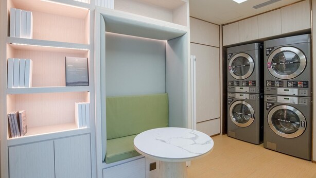 A laundry room with two stacked washing machines and a seating area with a table. - Ji Hotel (Beijing)